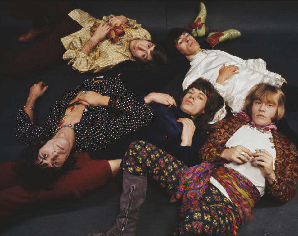 Keith Richards, Charlie Watts, Mick Jagger, Bill Wyman, and Brian Jones lying together on the floor in stylish, eclectic outfits