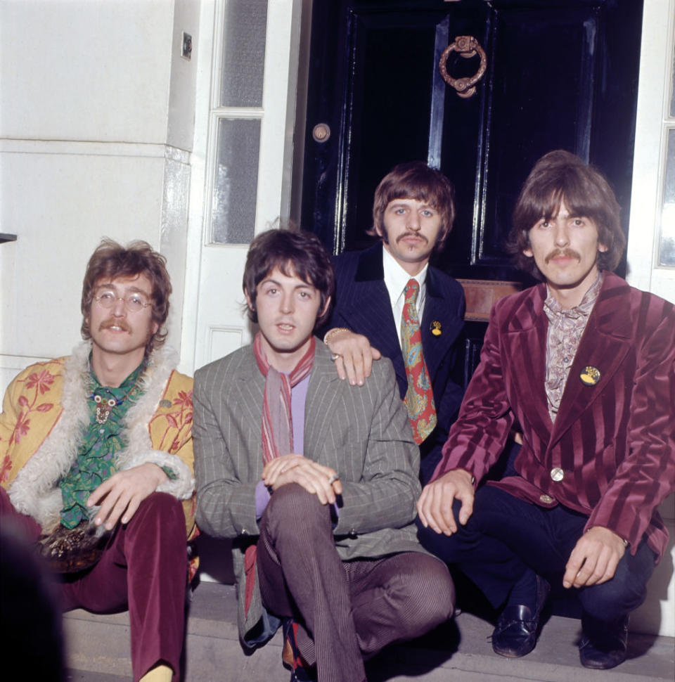 John Lennon, Paul McCartney, Ringo Starr, and George Harrison are sitting together on steps, dressed in fashionable late-1960s attire