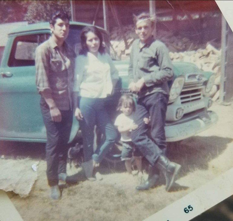 The family of Leonard Peltier stands around a blue pickup truck in an old photo.